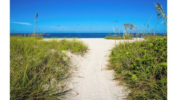 A sandy path leading to a beach with clear blue sky and ocean in the background. - Sand & Sea Oasis: Condo with Private Beach Access (Holmes Beach)