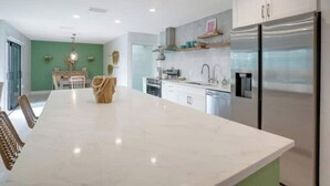 A modern kitchen with white cabinets, a large island, and stainless steel appliances. - Sand & Sea Oasis: Condo with Private Beach Access (Holmes Beach)
