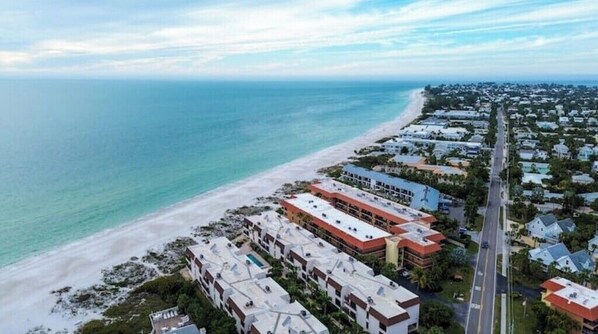 An aerial view of a coastal area with a beach, a road, and several buildings.