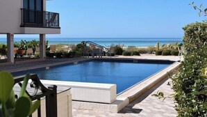 A swimming pool with a view of the ocean, surrounded by lounge chairs and potted plants. - Sand & Sea Oasis: Condo with Private Beach Access (Holmes Beach)