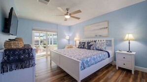 A bedroom with a bed, bedside tables, a ceiling fan, a TV, and a window. - Coastal Oasis: Cheerful 3Bedroom, Pool, Large Yard (Bradenton)