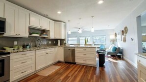 A modern kitchen with white cabinets, a dishwasher, and wooden flooring. - Coastal Oasis: Cheerful 3Bedroom, Pool, Large Yard (Bradenton)