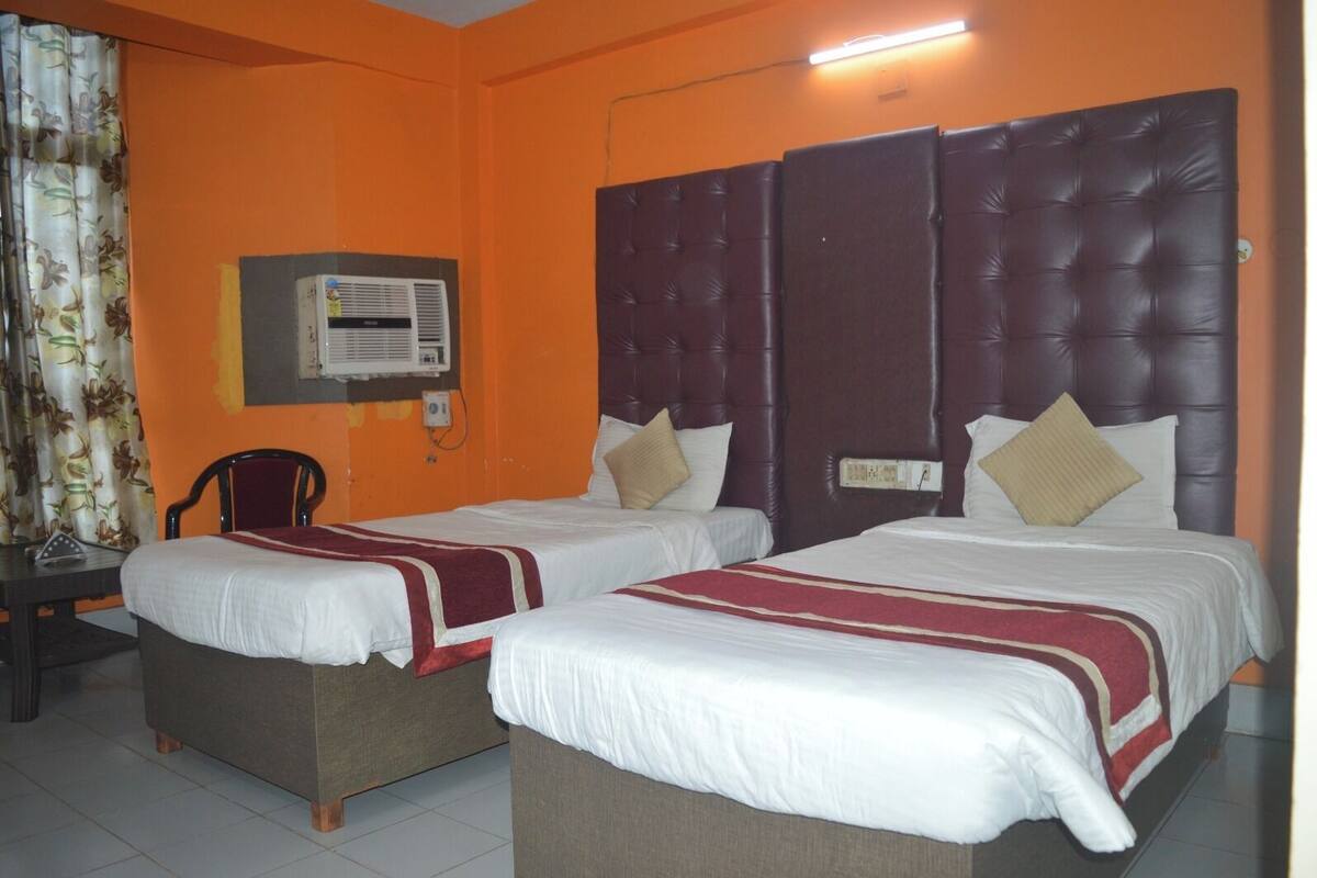 A hotel room with two beds, orange walls, a dark headboard, and a small table with a chair.