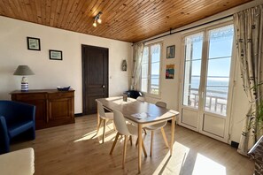 Quarto com teto de madeira, mesa de jantar com cadeiras, sofá, armário e vista através de amplas janelas.