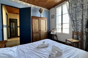 Une pièce comprenant un lit, une armoire en bois, une chaise et une fenêtre avec des rideaux.