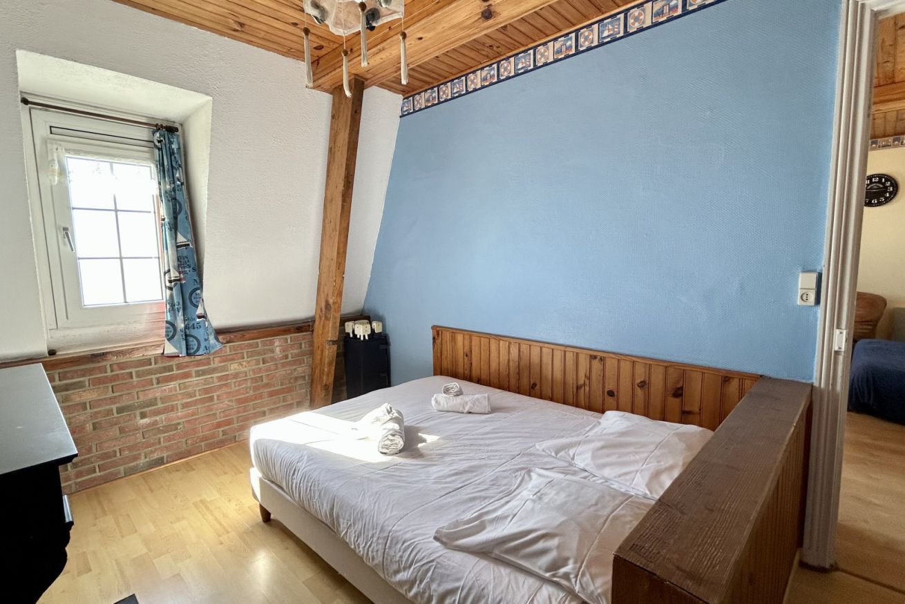 A bedroom with a bed, a window with curtains, a wooden ceiling, and a brick wall.
