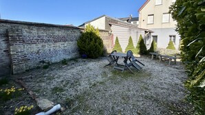 Un patio de grava con una mesa y sillas, un muro de ladrillo y un edificio con tejado rojo.