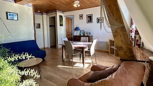 Una habitación con techo de madera, una mesa de comedor con sillas, un sofá azul y un sillón de cuero marrón.