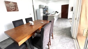 Un comedor con mesa de madera y sillas negras, una cocina con electrodomésticos modernos y una estatua de Buda en la pared.
