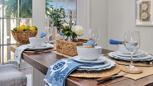 A dining table set with white plates, bowls, and glasses, accompanied by woven placemats and a basket of lemons. - Charming Coastal Cottage on St. Simons Island (St. Simons Island)