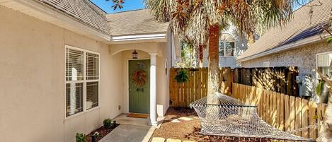 A residential property with a front yard, a wooden fence, a hammock, and a door marked with the number 418.