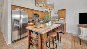 A modern kitchen with a central island, stainless steel appliances, wooden cabinets, and a large window. - Charming Coastal Cottage on St. Simons Island (St. Simons Island)