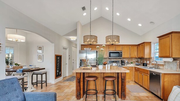 A spacious kitchen with wooden cabinets, a central island with stools, and pendant lighting. - Charming Coastal Cottage on St. Simons Island (St. Simons Island)