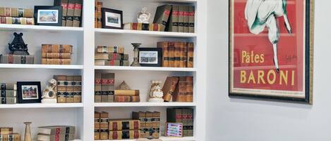 Una habitación con una mesa redonda, cuatro sillas, una estantería llena de libros y un cartel enmarcado en la pared.
