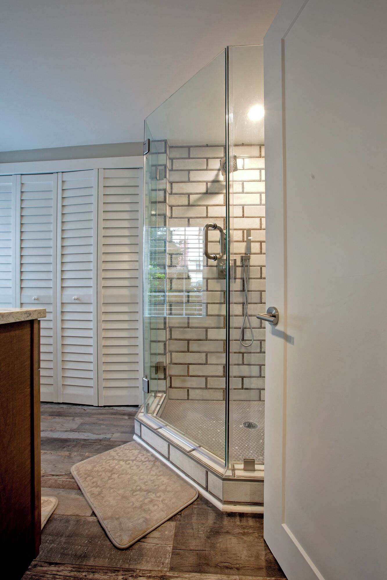 A modern bathroom with a glass shower enclosure, a wooden floor, and a white tiled wall.