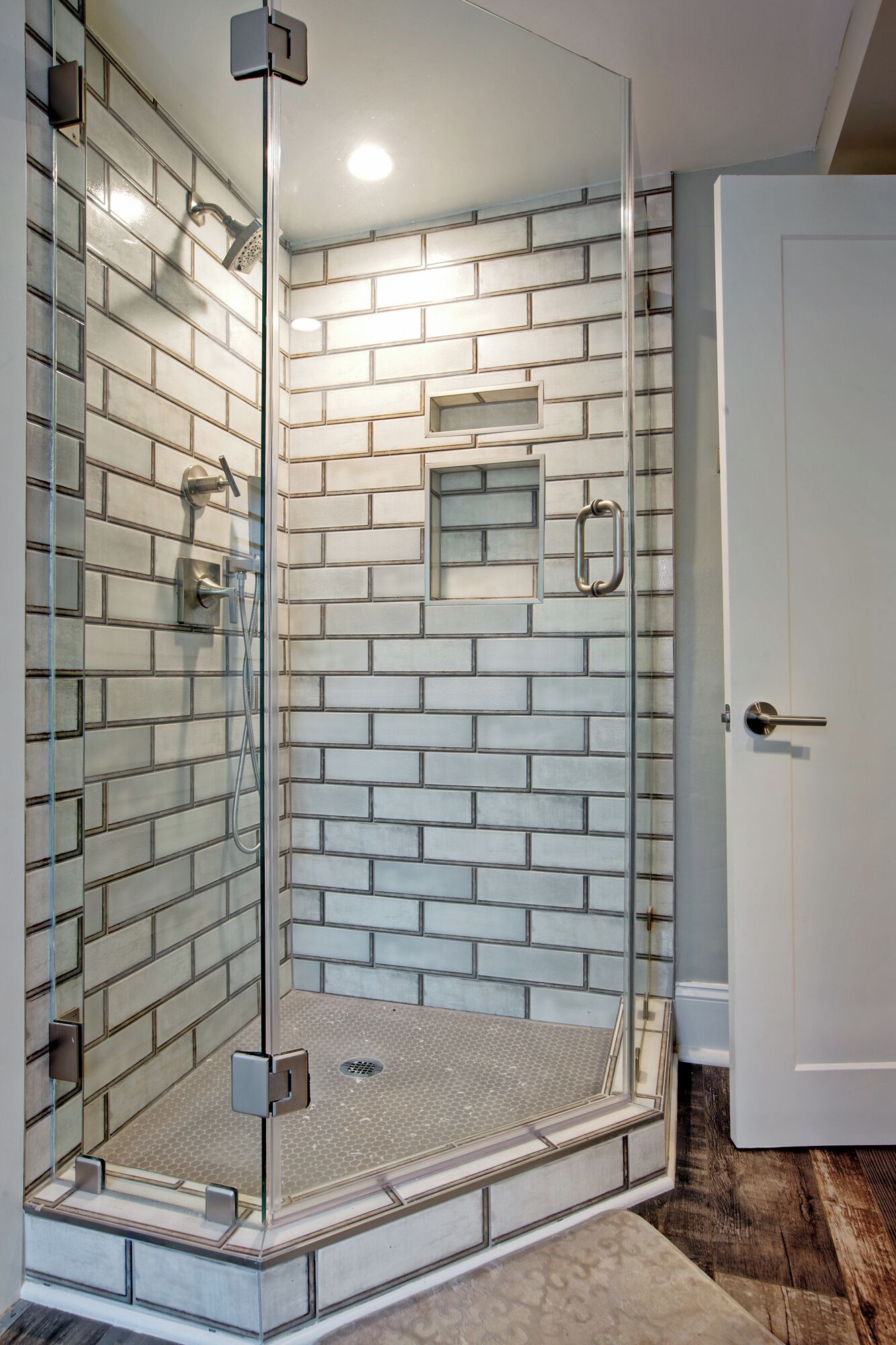 A glass-enclosed shower with a brick-patterned wall, a small shelf, and a door to the right.