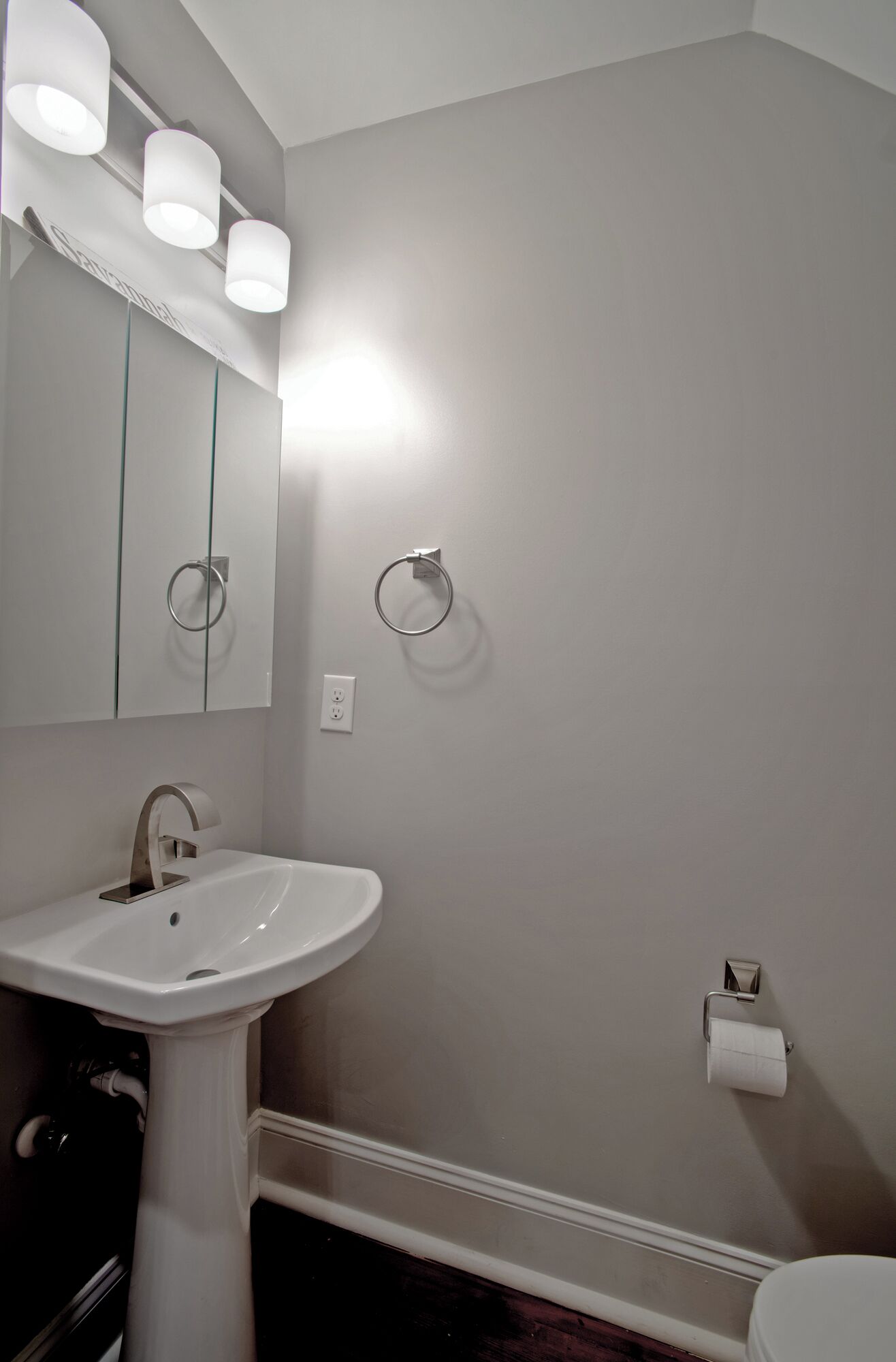 A bathroom with a pedestal sink, a mirror, and a toilet.