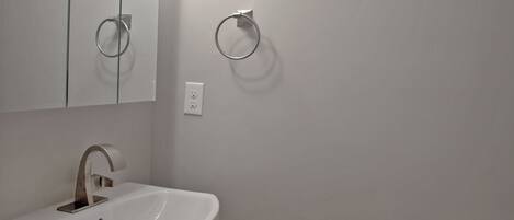 A bathroom with a pedestal sink, a mirror, and a toilet.