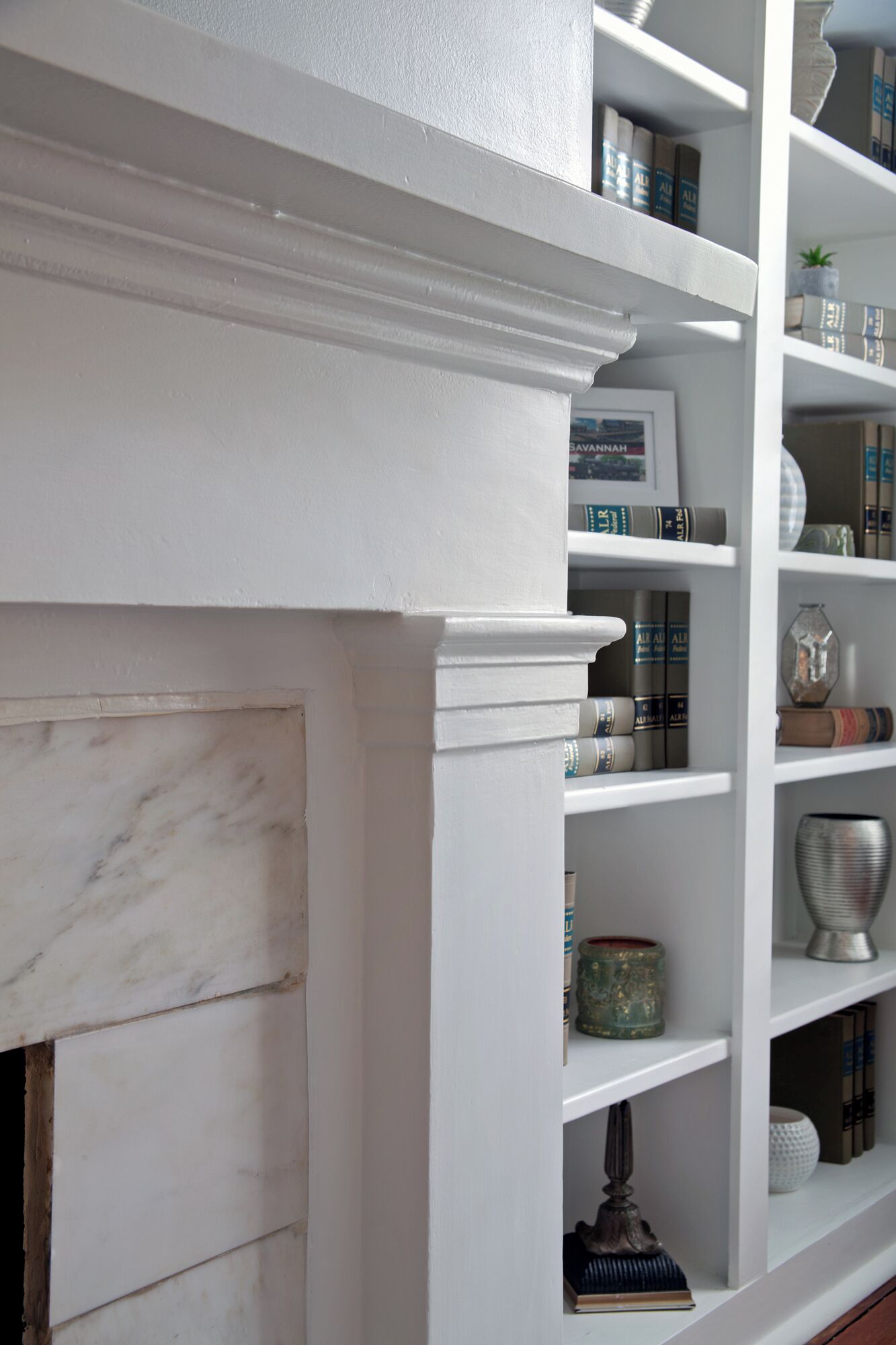A white bookshelf with a marble fireplace.