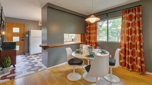 A modern kitchen with a built-in refrigerator, a dining area with a round table and white chairs, and a window with orange curtains. - No. 1 Rosetree Suites - 3 Beds - Perfect Family Location in Calgary (Calgary)
