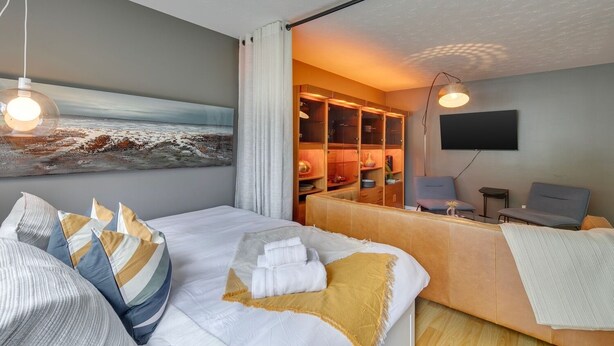 A modern hotel room with a bed, a desk, a television, and a large painting of a beach scene. - No. 1 Rosetree Suites - 3 Beds - Perfect Family Location in Calgary (Calgary)