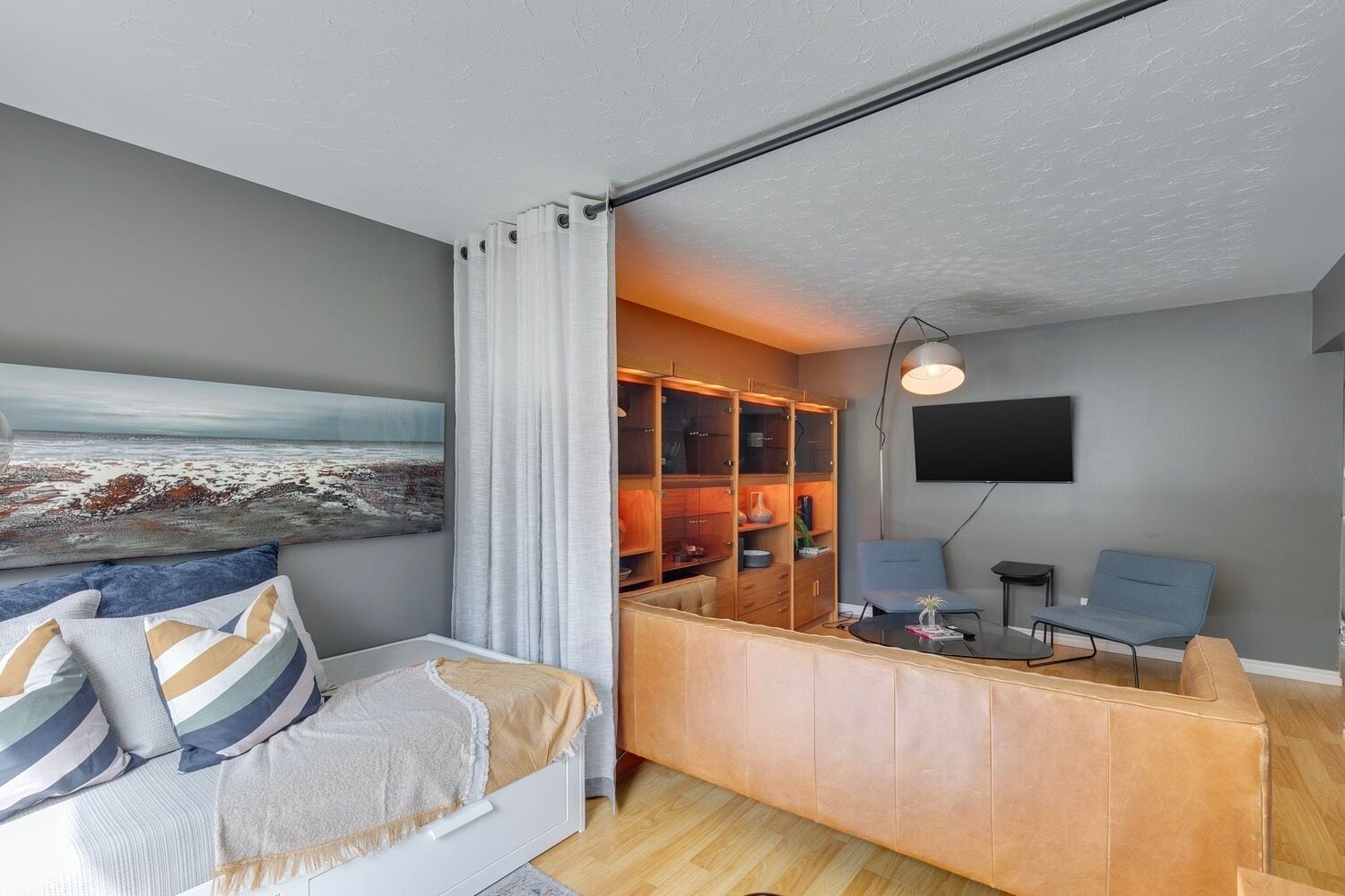 Habitació moderna amb llit, zona de seients amb televisor i un armari de fusta.