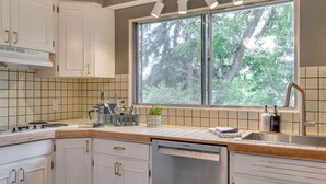 A modern kitchen with white cabinets, a Bosch dishwasher, a window with a view of trees, and a sink with soap dispensers. - No. 1 Rosetree Suites - 3 Beds - Perfect Family Location in Calgary (Calgary)