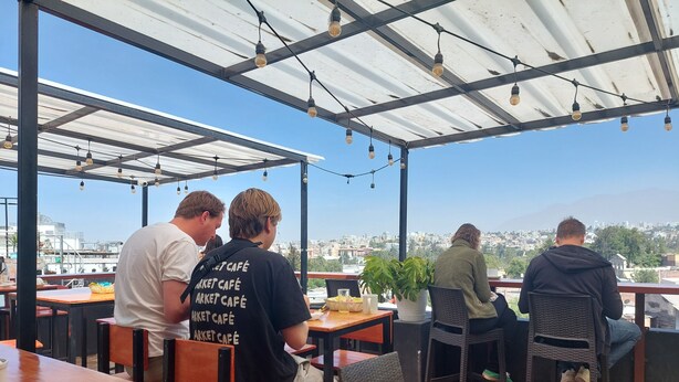 A rooftop café with tables and chairs, a view of the city, and string lights. - Lonko Hostel Arequipa (Arequipa)