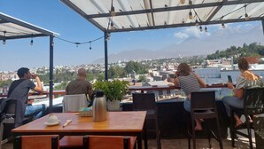 An outdoor seating area with tables and chairs, a view of a cityscape and mountains, and string lights hanging from the ceiling. - Lonko Hostel Arequipa (Arequipa)