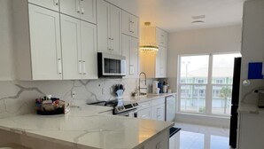 A modern kitchen with white cabinets, a marble countertop, and gold bar stools. - 4 Beds/4Baths ROOFTOP! Gorgeous MODERN 360 degree views STEPS TO THE BEACH! (Pensacola Beach)