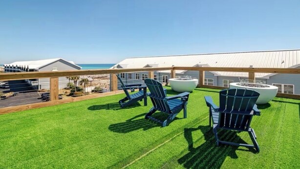 A rooftop terrace with artificial grass, three Adirondack chairs, a fire pit, and a view of the ocean. - 4 Beds/4Baths ROOFTOP! Gorgeous MODERN 360 degree views STEPS TO THE BEACH! (Pensacola Beach)