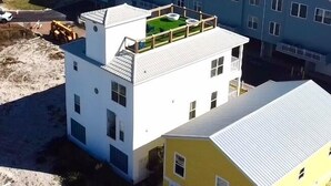 A coastal residential area with houses featuring white and yellow exteriors, a rooftop garden, and a view of the ocean. - 4 Beds/4Baths ROOFTOP! Gorgeous MODERN 360 degree views STEPS TO THE BEACH! (Pensacola Beach)