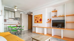 A compact living space with a kitchenette, dining area, and a TV on a shelf.