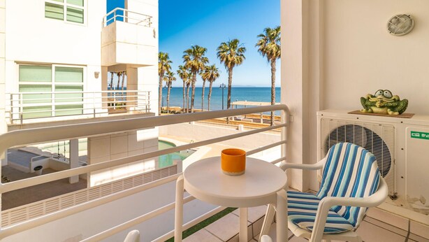 A balcony with a view of the sea, a chair, a small table with a cup, and an air conditioning unit.