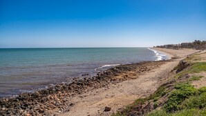 A beach with a rocky shoreline, a clear sky, and a distant view of buildings.