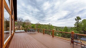 Una terraza de madera con barandilla, muebles de exterior y vistas a un paisaje montañoso.