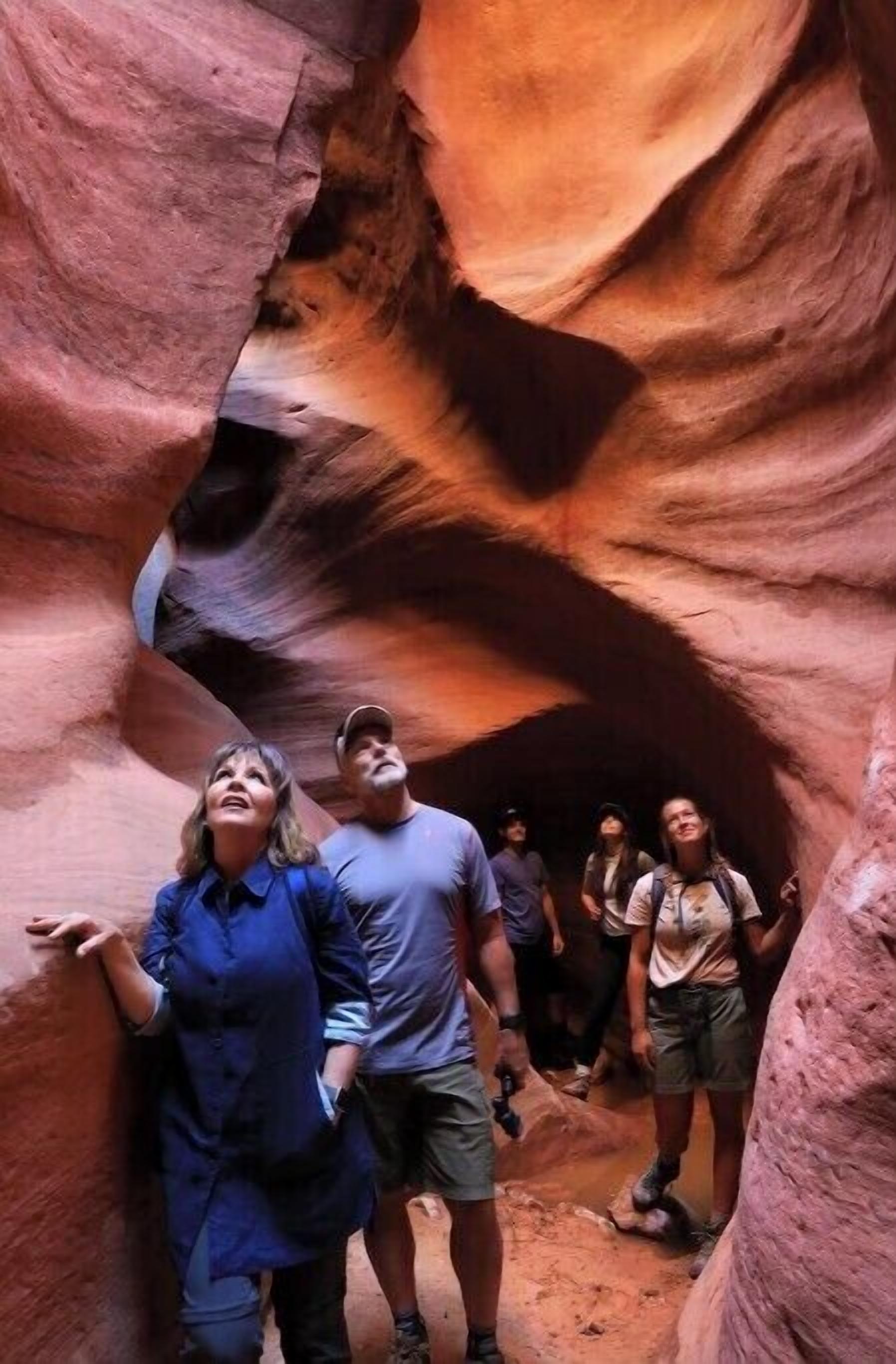 A group of people inside a narrow canyon with reddish rock walls.