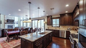 A spacious kitchen with dark wood cabinets, a granite countertop island, stainless steel appliances, and pendant lighting. - Zion Views- The Retreat +Resort Access (Orderville)