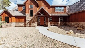 A large, rustic wooden house with a stone foundation, multiple entry points, and a gravel driveway. - Zion Views- The Retreat +Resort Access (Orderville)