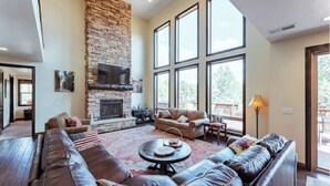 A spacious living room with a stone fireplace, leather sofas, and large windows. - Zion Views- The Retreat +Resort Access (Orderville)