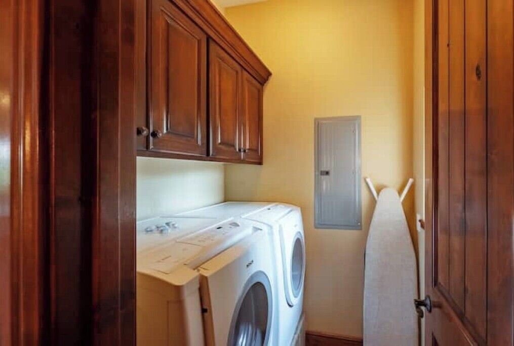 A laundry room with a front-loading washer and dryer, wooden cabinets, and a drying rack.