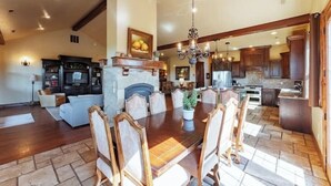 A spacious living area with a dining table and chairs, a fireplace, and a kitchen in the background.