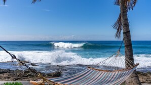 A hammock tied to a palm tree on a rocky beach with waves crashing nearby. - Tropical Oceanfront Paradise (Waianae)