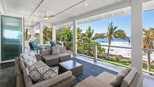 A spacious balcony with a view of the beach and ocean, furnished with a sofa, chairs, and a table. - Tropical Oceanfront Paradise (Waianae)
