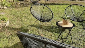 Un'area relax all'aperto con sedie e tavoli in metallo, un piccolo albero e un edificio con tetto in tegole sullo sfondo.