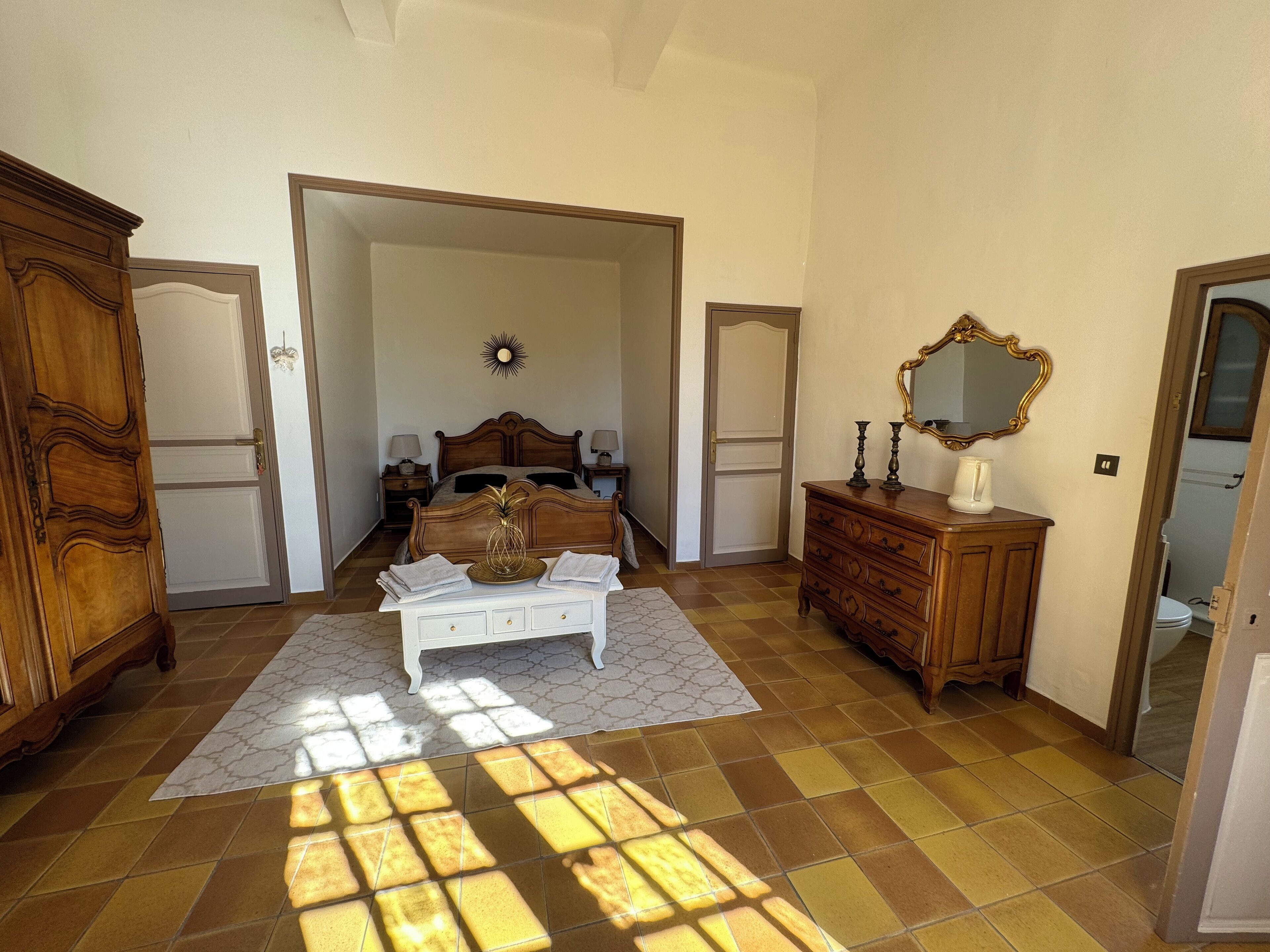 A hotel room with a bed, dresser, and mirror. There is a door leading to another room.