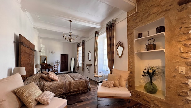 Un'ampia camera da letto con un letto grande, un angolo relax con divano e poltrona, una parete decorata in pietra e un soffitto in legno.