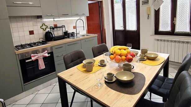 Een moderne keuken met grijze kastjes, een houten eettafel en een schaal fruit.