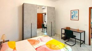 Een slaapkamer met een bed, een bureau, een stoel, een kledingkast en een plafondlamp.