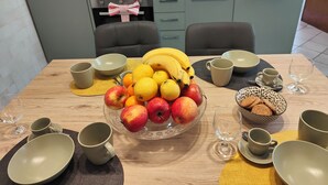 Een eettafel gedekt met fruit, kommen en kopjes in een moderne keuken.